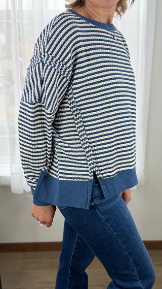 Person wearing a blue and white striped sweater with blue pants in a room with white curtains.