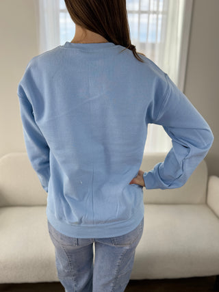 Person wearing a light blue sweatshirt in a neutral indoor setting