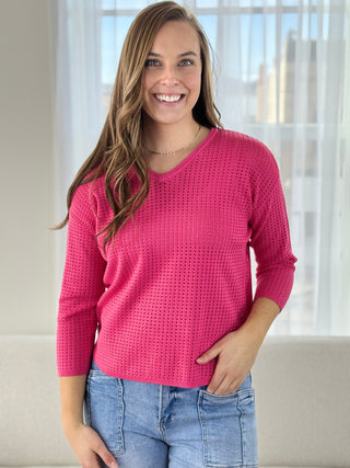 Woman wearing a pink sweater and blue jeans indoors with a neutral background