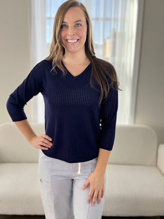 Woman wearing a navy blue sweater and light gray pants indoors.