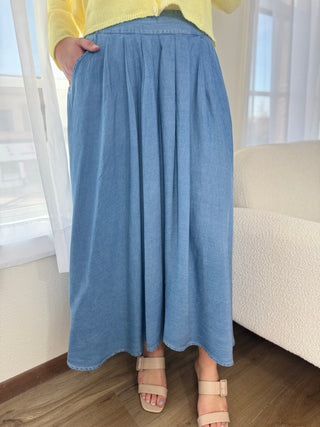 Person wearing a blue denim skirt indoors with a neutral background