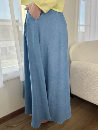 Person wearing a long blue skirt and yellow top in a room with a couch and window.