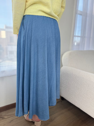 Person wearing a yellow sweater and blue denim skirt in a room with a white sofa and large window.