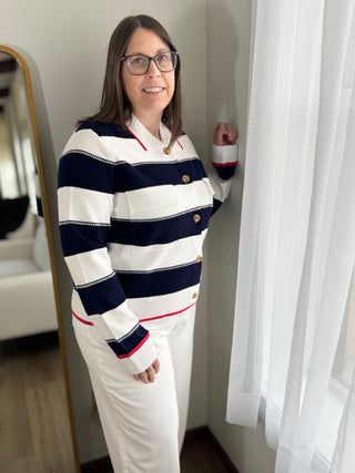 Woman wearing a striped shirt and white pants standing in a room with a mirror and curtains.