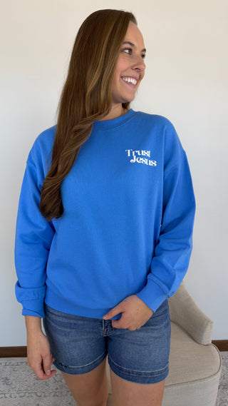 Woman wearing a blue sweatshirt with text, standing against a plain wall.