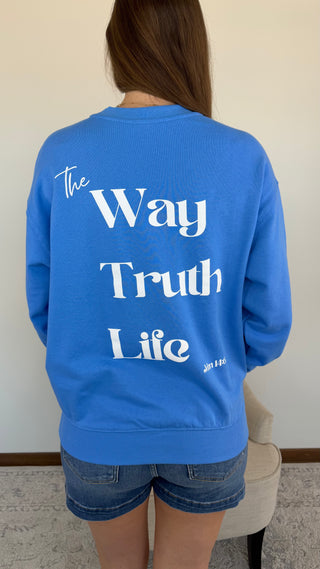 Person wearing a blue sweatshirt with text on the back, standing against a plain wall.