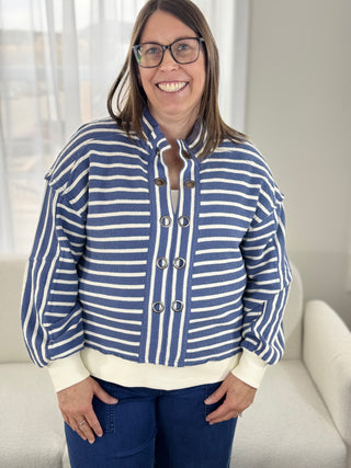 Person wearing a blue and white striped jacket with a white shirt and blue jeans indoors.
