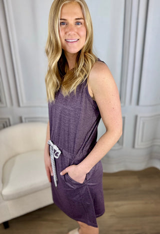 Woman wearing a purple sleeveless dress with a belt in a neutral setting
