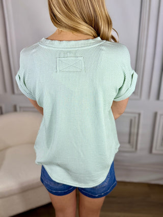 Person wearing a light green ribbed top and blue shorts in a neutral setting