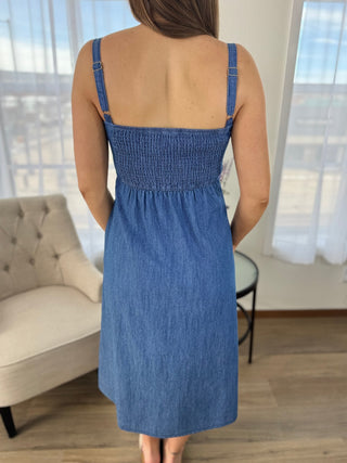 Woman wearing a blue denim dress in a room with a couch and curtains.
