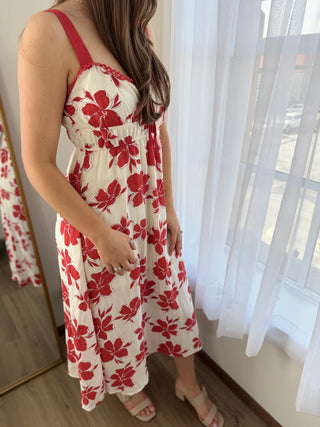 Lady looking out window wearing a red floral sundress.