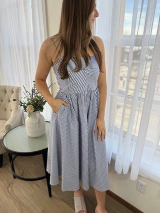 Woman wearing a blue and white striped dress in a room with white curtains and a table.