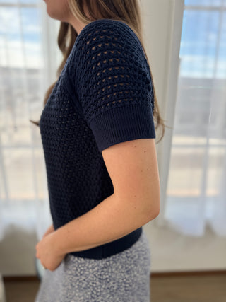 Person wearing a navy blue knitted cardigan in a bright room with large windows.