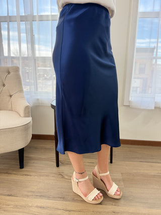 Person wearing a blue skirt and white sandals in a room with large windows.