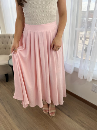Person wearing a light pink skirt in a room with a couch and window.