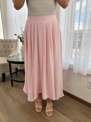 Person wearing a pink skirt in a room with a couch and window.