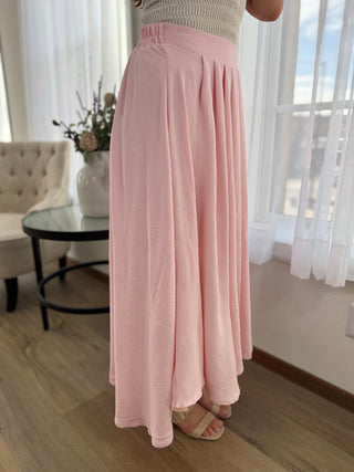 Person wearing a long pink skirt in a room with light-colored walls and wooden flooring.