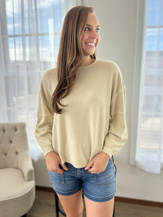 Woman wearing a beige sweater and denim shorts in a room with large windows.