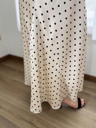 White skirt with black polka dots worn by a person on a wooden floor.