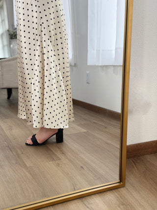 Person wearing a polka dot dress standing in front of a mirror on a wooden floor.