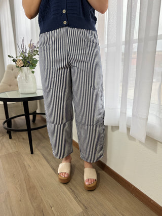 Person wearing black and white striped pants in a room with light wood flooring and white curtains.