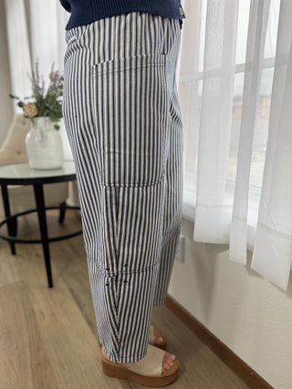 Person wearing black and white striped pants in a room with light wood flooring and sheer curtains.