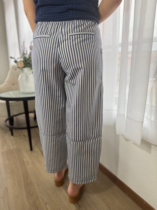 Person wearing black and white striped pants in a room with light wood flooring and white curtains.