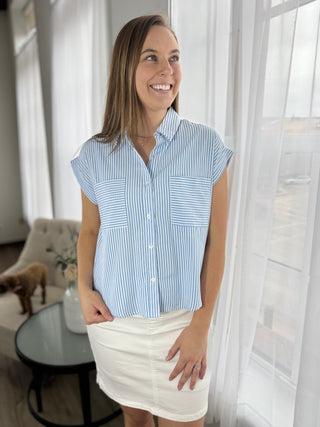 Woman wearing a blue striped shirt and white skirt in a bright room.