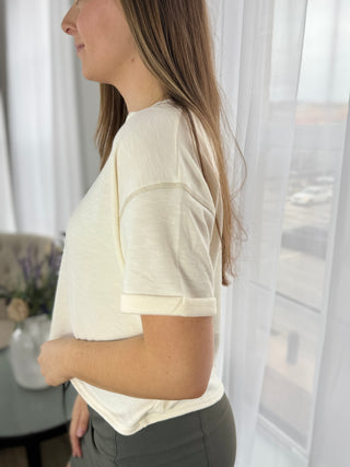 Woman wearing a white t-shirt in a casual setting with light curtains in the background