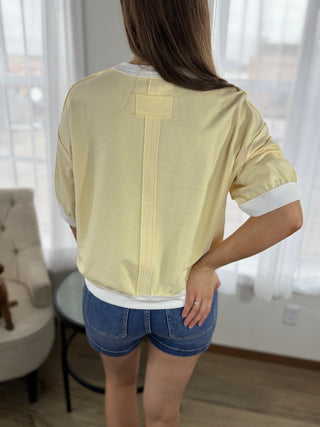 Person wearing a light yellow shirt with a white collar and blue shorts indoors.