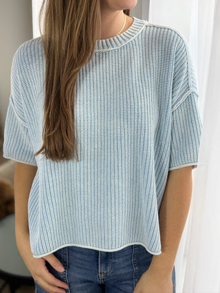 Person wearing a light blue knitted sweater with a neutral background