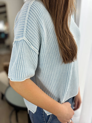 Person wearing a light blue knitted sweater with a blurred indoor background