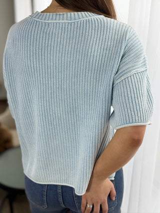 Light blue knitted sweater worn by a person, with a blurred background