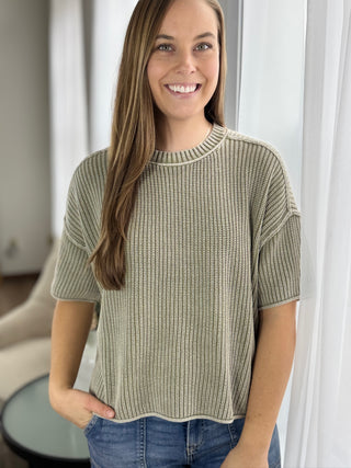 Woman wearing a green knitted sweater in a room with white curtains.