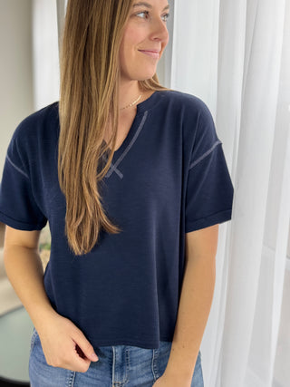 Woman wearing a navy blue t-shirt with white curtains in the background