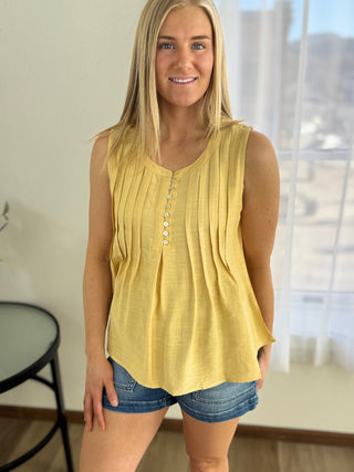 Woman wearing a yellow sleeveless top with buttons, standing indoors.