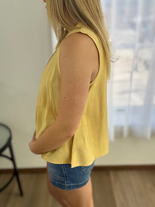 Person wearing a yellow sleeveless top and denim shorts in a room with a blurred background