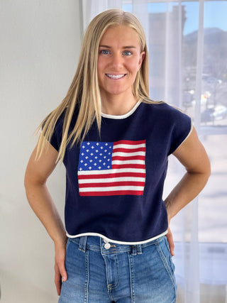 Woman wearing a navy blue sleeveless top with an American flag design, standing indoors.