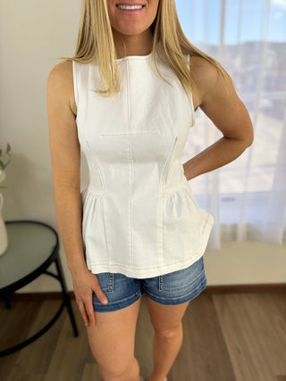Woman wearing a white sleeveless top and denim shorts indoors.