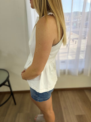 Woman wearing a white sleeveless top and denim shorts in a room with a window.