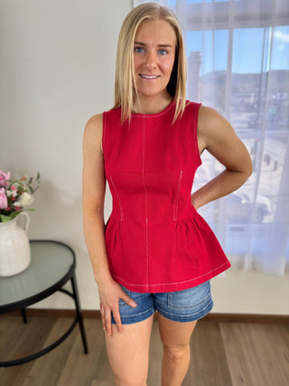 Woman wearing a red sleeveless top and denim shorts indoors.