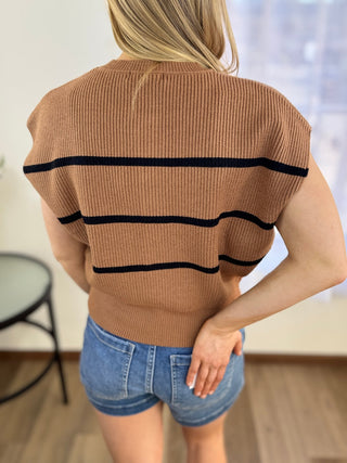 Person wearing a brown ribbed sweater with black stripes and denim shorts indoors.