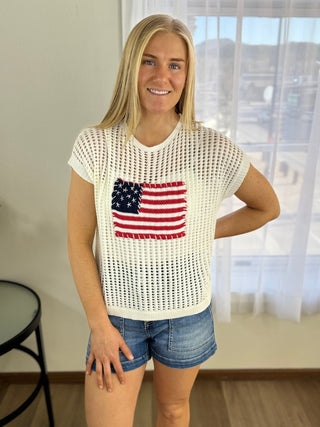 Woman wearing a white mesh top with an American flag design indoors.
