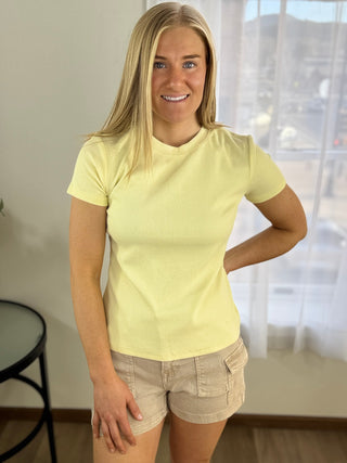 Woman wearing a yellow t-shirt and beige shorts indoors.