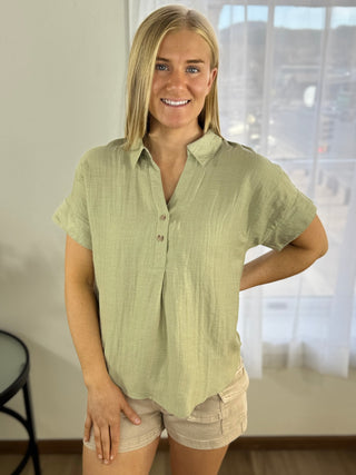 Woman wearing a light green shirt and beige shorts indoors.