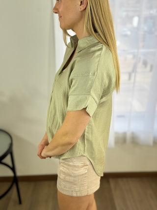 Woman wearing a light green shirt and beige shorts indoors.
