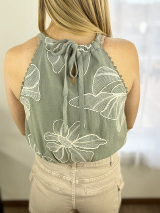 Green floral embroidered top worn by a person with a blurred background