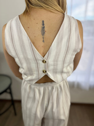 Person wearing a white sleeveless top with buttons and cut-out design, standing indoors.