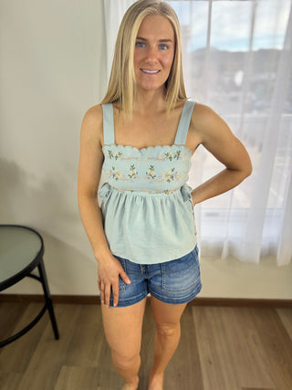 Woman wearing a light blue top with floral embroidery and denim shorts indoors.