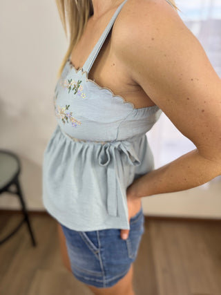 Light blue sleeveless top with floral embroidery worn by a person, standing indoors.